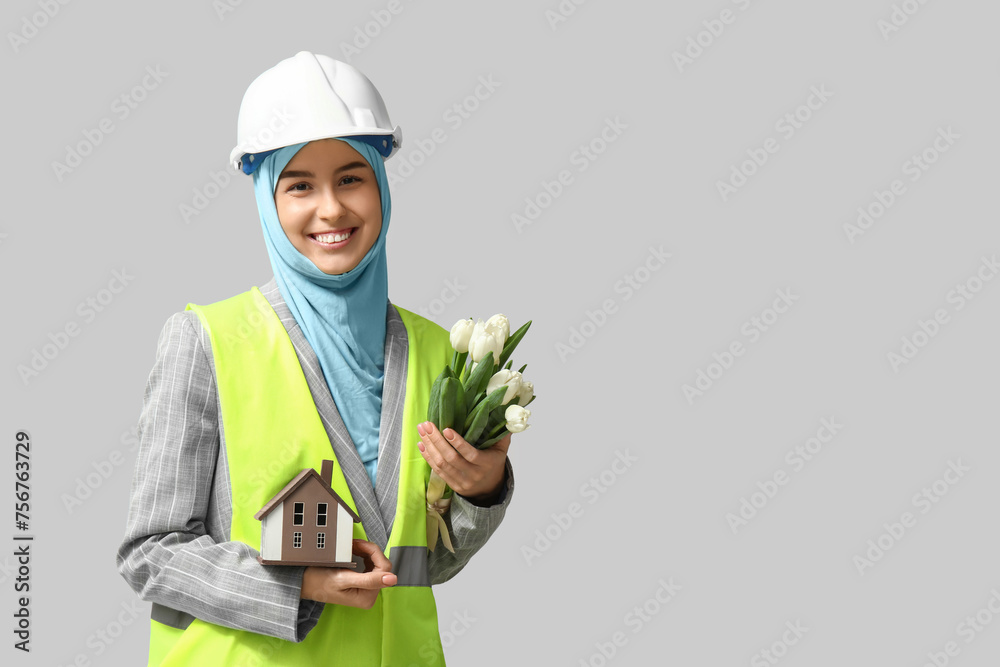 Muslim female construction worker with toy house and tulips on white background. Women's Day celebration Muslim female construction worker with toy house and tulips on white background. Women's Day celebration