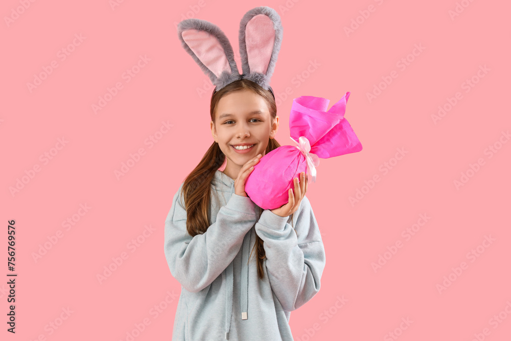 Cute little girl with Easter bunny ears and gift on pink background