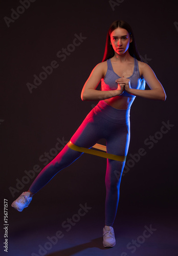 A slender female bodybuilder in a lilac tracksuit is doing an exercise with an expander on her legs, doing cardio. Sports concept, fat burning and healthy lifestyle. © Dimid