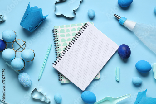 Blank notepads for recipes with pen, baking tools and Easter eggs on blue background