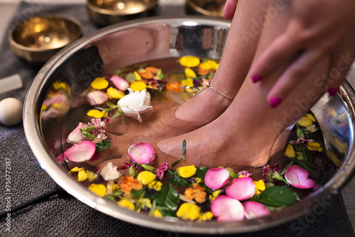 Foot massage and feet therapy in spa salon in bowl full of pentals of flowers and rose. Pedicure and aromatherapy. Closeup.
