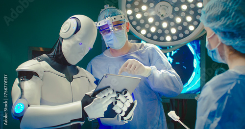 Robot holding digital tablet helps doctor to perform surgical operation in modern hospital. Teamwork of professional medical surgeons in operating room. Concept of modern medicine.