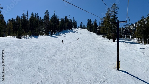 Looking across mountain slope with anonymous, silhouetted skiers descending, chair lift on the right. Mammoth Mountain, California