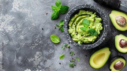 A fresh guacamole in a stone bowl, surrounded by ripe avocados and herbs on a textured gray surface.