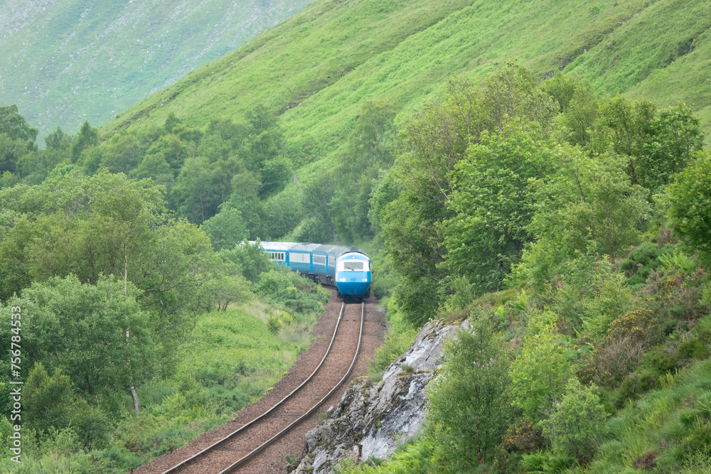 Blue passenger train snakes through the green valleys of the Scottish Highlands