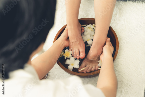 Woman indulges in blissful foot massage at luxurious spa salon while masseur give reflexology therapy in gentle day light ambiance resort or hotel foot spa. Quiescent photo
