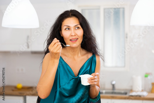 Portrait of positive asian woman eating yogurt at home. Woman having breakfast with dairy product.