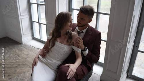 Bride in wedding dress groom in suit sit by window, happy making gestures