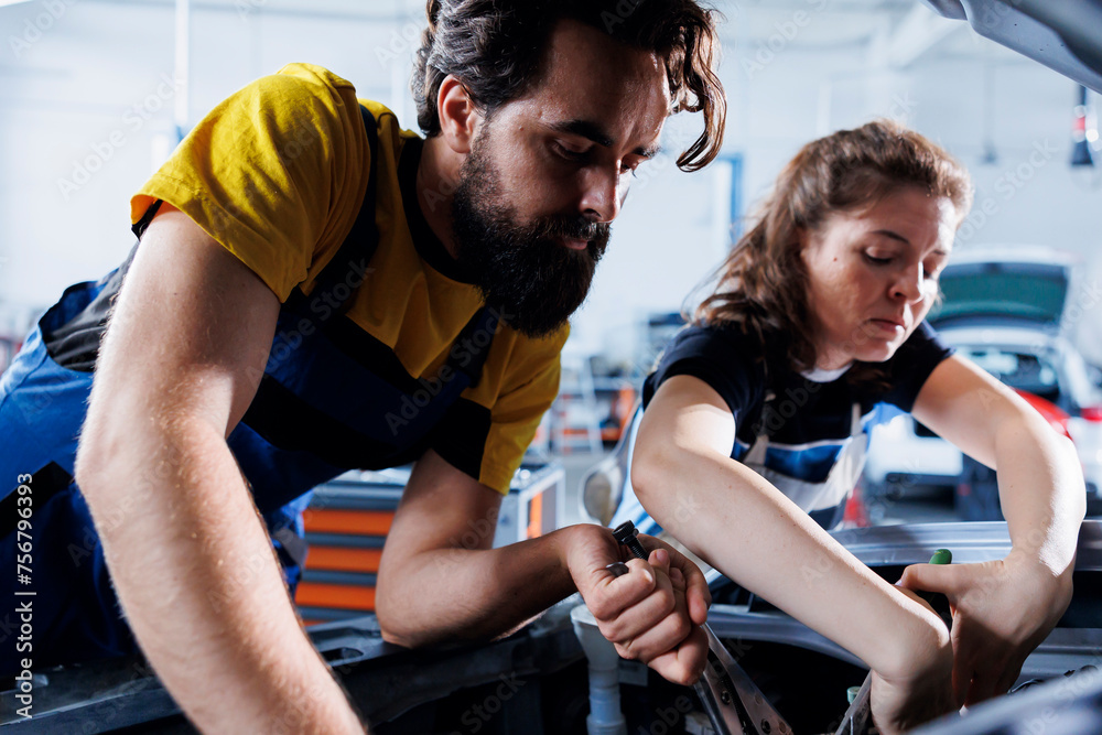 Repairman and coworker collaborating on servicing broken vehicle, checking for faulty battery. Knowledgeable mechanics in auto repair shop working together on fixing car, discussing best options