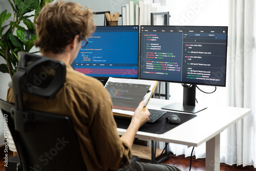 Working IT developer reading coding on document paper software with screens pc at modern office on coding application screens, creating updated program firmware information version concept. Gusher.