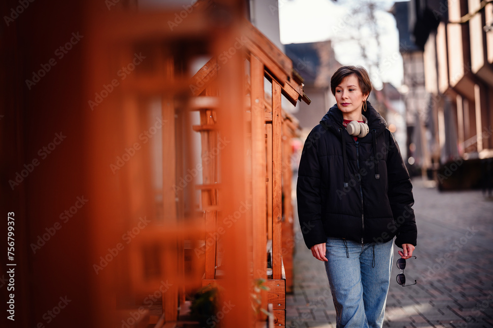 A young woman with headphones around her neck enjoys a relaxed stroll, her presence adding a contemporary layer to the historical town backdrop