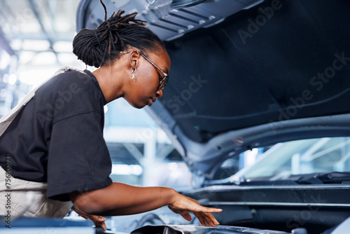 BIPOC woman in car service using professional mechanical tool to repair broken ignition system. Skilled specialist in garage fixing client automobile, ensuring optimal automotive performance