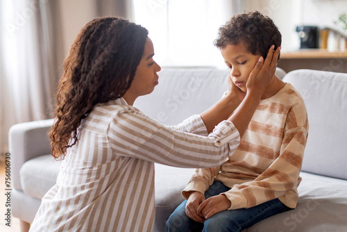 Caring black mother gently cradling her preteen son's face, comforting upset kid © Prostock-studio