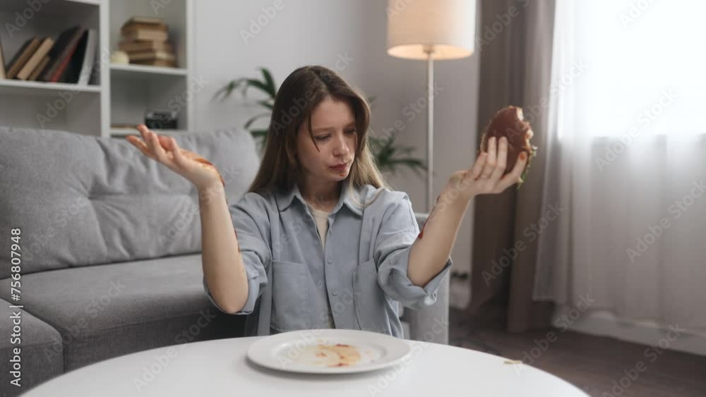 Portrait of funny happy young woman eating burger with great pleasure while ketchup flows down the hands at home Excited hungry female biting hamburger enjoying fast junk food indoors Portrait of funny happy young woman eating burger with great pleasure while ketchup flows down the hands at home Excited hungry female biting hamburger enjoying fast junk food indoors