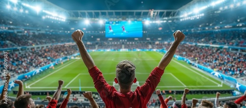 Modern football Stands buzzing with An ecstatic audience raising their arms in the foreground, with a grass field and a large screen in the background