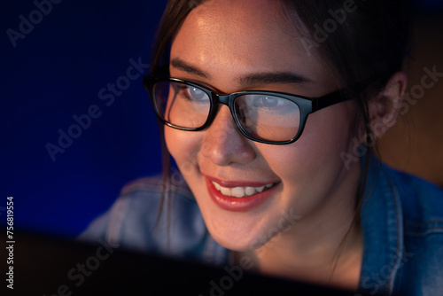 Portrait young beautiful Asian creative with glasses of smiling face looking on pc to search project creator social media online  planning strategy creator at neon modern office at night. Stratagem.