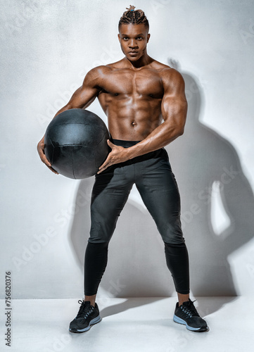 Muscular man doing twist exercise with med ball. Photo of man with great physique on gray background. Strength and motivation