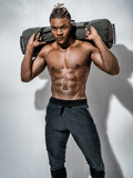 Sporty man working out with heavy sandbag. Photo of man with naked torso on grey background. Strength and motivation