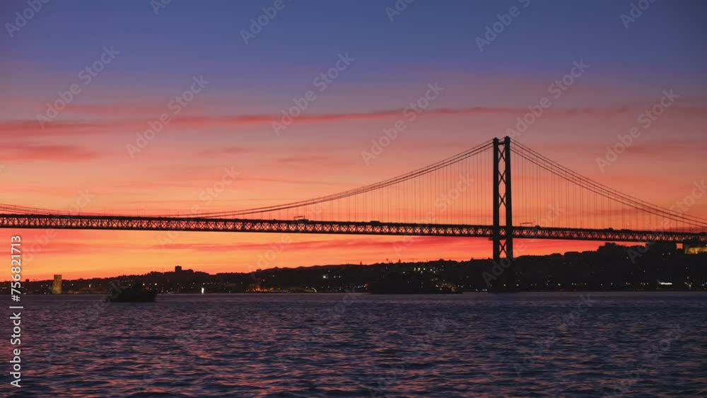 View of 25 de Abril Bridge famous tourist landmark of Lisbon connecting Lisboa and Almada on Setubal Peninsula over Tagus river with passing tourist yacht boat silhouette on sunset. Lisbon, Portugal View of 25 de Abril Bridge famous tourist landmark of Lisbon connecting Lisboa and Almada on Setubal Peninsula over Tagus river with passing tourist yacht boat silhouette on sunset. Lisbon, Portugal