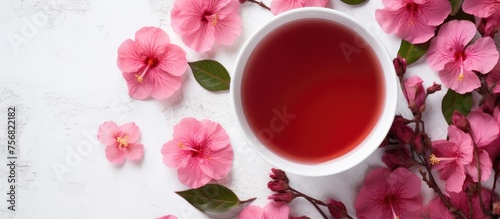 A cup of red tea sits on a table adorned with pink flowers, creating a beautiful contrast between the liquid and the delicate petals