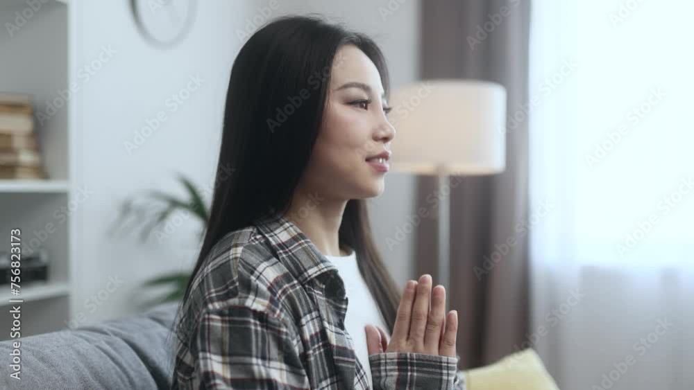 Relaxed young asian woman meditate and breathe slowly while make yoga sitting on couch at home Calm inspired female with closed eyes take break while resting for peaceful mind alone