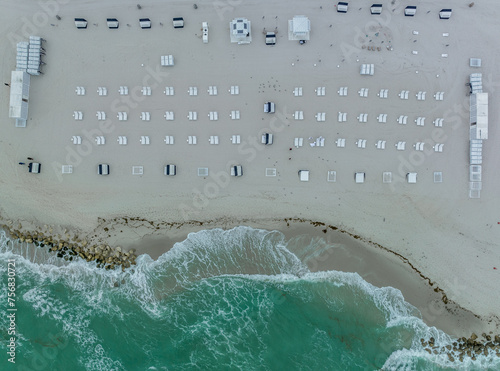 Aerial view of lounge beach chairs laid out in a patterns on Miami beach as the ocean waves crash