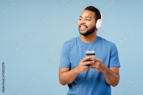 Portrait of smiling handsome man wearing headphones, holding mobile phone, listening to musi