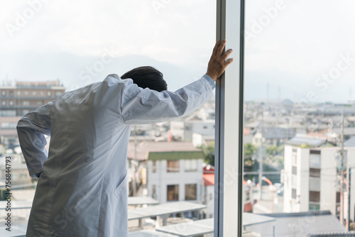 ガラス窓にもたれかかる男性医者・医師・ドクター（ストレス・過労・疲労・悩む・考える）
 photo