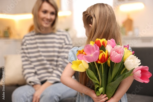 Little girl hiding bouquet of tulips for mom at home, selective focus. Happy Mother's Day