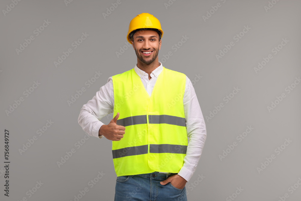 Engineer in hard hat showing thumb up on grey background