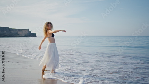 Performer practicing contemporary choreography on sea waves summer morning.