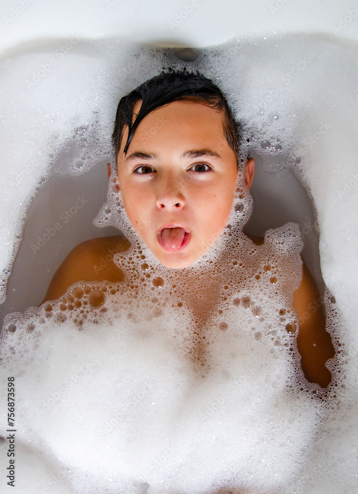 Young boy in bubble bath playfully sticking out his tongue