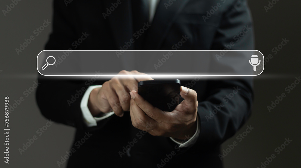 A man in a suit is using a cell phone with a search bar on the screen