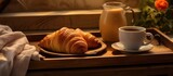 The tray contains a croissant and a cup of coffee, showcasing a perfect combination of food and drink in elegant tableware