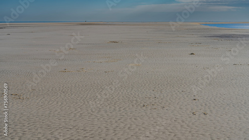 The seabed was exposed at low tide. The undulating sand stretches to the horizon. The ocean is visible in the distance. Clouds in the blue sky. Madagascar. Morondava. The Mozambique Channel.