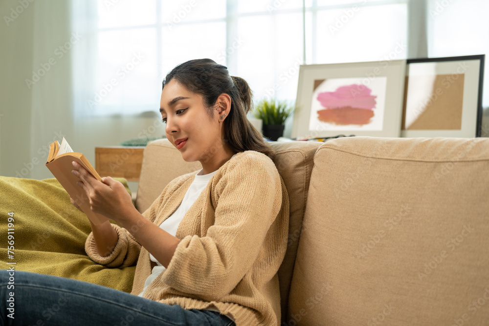 © Chanakon - Asian beautiful woman sitting reading book on cozey couch sofa in living room with sun light morning. People female stay home part time relax at home. © Chanakon - Asian beautiful woman sitting reading book on cozey couch sofa in living room with sun light morning. People female stay home part time relax at home.