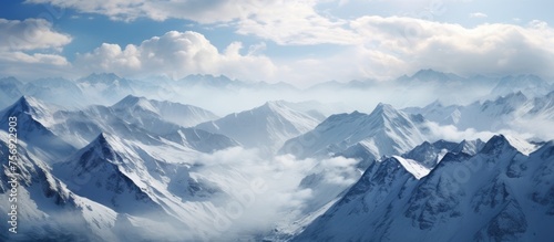 A majestic mountain range shrouded in snow and clouds with a clear blue sky in the background, creating a stunning natural landscape