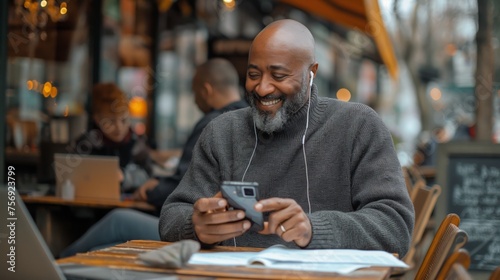 A cheerful, bearded senior man is enjoying his time using a smartphone at an outdoor cafe, with a blurred background of city life and fellow patrons © foxyburrow