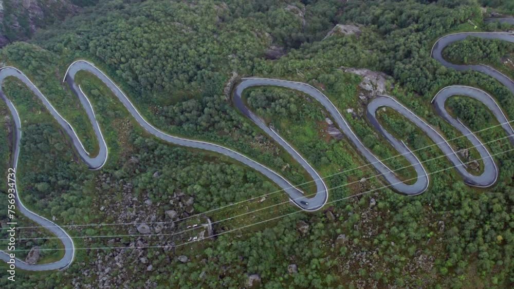 Close aerial top down view of a tight twisting serpentine road as it snakes up a steep, forest covered valley side, next to a Fjord in Norway. Close aerial top down view of a tight twisting serpentine road as it snakes up a steep, forest covered valley side, next to a Fjord in Norway.