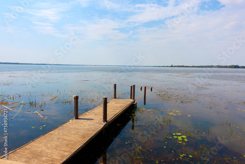 Fototapeta Naklejka Na Ścianę i Meble -  A wooden pier on a large pond with small cornices surrounding it.
