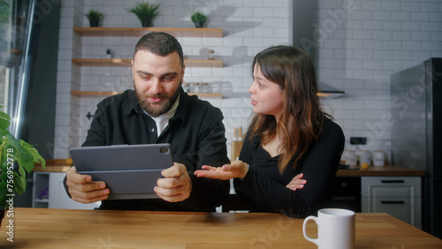 Young lovers sitting in the kitchen, man playing a racing mobile game on tablet computer woman messing with the her boyfriend 