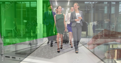 Image of hands using laptop with green screen over colleagues walking in corridor with suitcases
