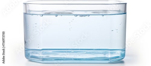 A rectangular piece of drinkware made of plastic, filled with liquid water, sits on a white surface, reflecting light and creating a serene scene photo