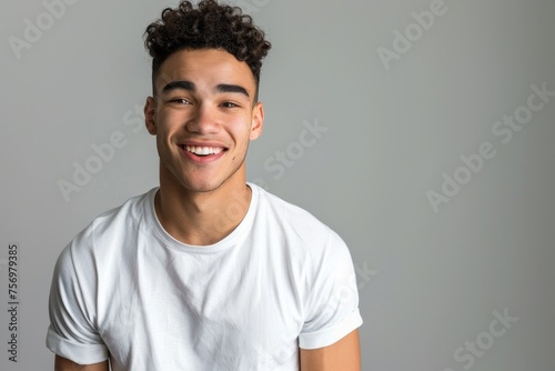 Portrait of a cheerful young man with curly hair, wearing a white t-shirt, against a neutral background. Ideal for lifestyle and diversity themes.