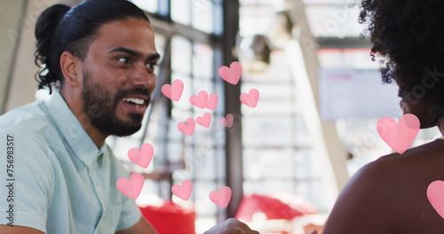Pink heart icons against african american couple holding hands while sitting in a restaurant