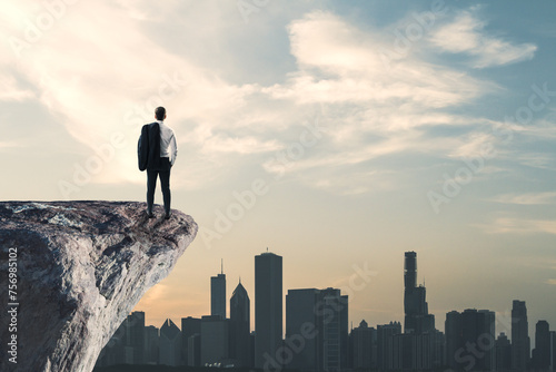 Back view of businessman standing on cliff edge on bright blue sky with mock up place background. Future  success and tomorrow concept.