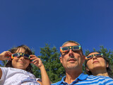 Mother, father and daughter looking at the sun during a solar eclipse on a country park, family outdoor activity