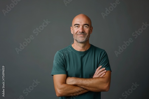 Smiling mature bald man with arms crossed wearing green t-shirt on grey background, concept of contentment and confidence photo