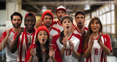 Front view of a group of sports fans wearing red and white jerseys cheering in a gym