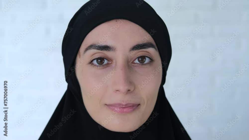 Muslim woman in black hijab smiles at camera Close-up: face of Muslim woman in black hijab - beautiful brown eyes, slight smile on lips, graceful oval face Concept: captivating smile of Muslim woman Muslim woman in black hijab smiles at camera Close-up: face of Muslim woman in black hijab - beautiful brown eyes, slight smile on lips, graceful oval face Concept: captivating smile of Muslim woman